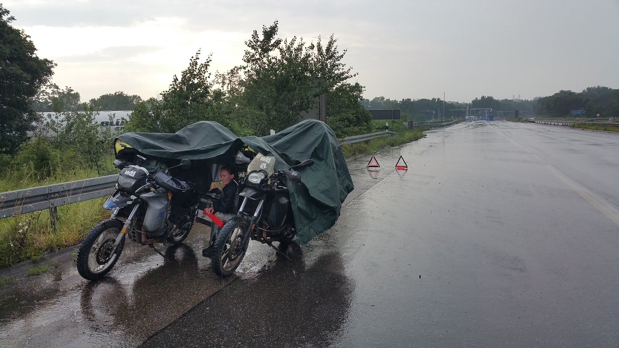 The Pack Track broke down in Germany in the rain. Huddled under the tarpaulin slung over the motorbikes waiting for roadside assistance.